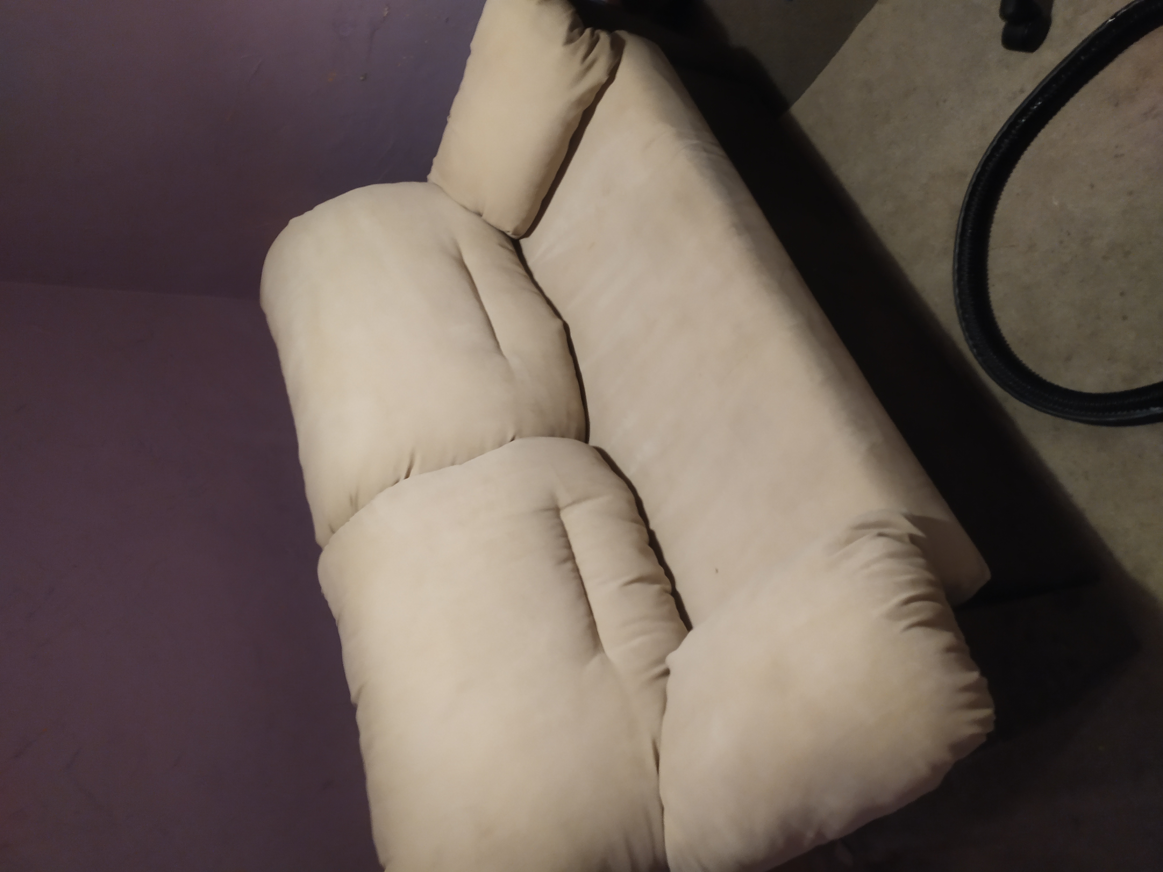 Beżowa, dwuosobowa kanapa z poduszkami w Olsztynie, widoczny wąż od odkurzacza.