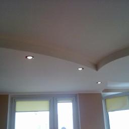 Krzysztof - Podwieszany sufit z oświetleniem punktowym, widok z dołu na fragment pokoju z dwoma oknami z roletami.