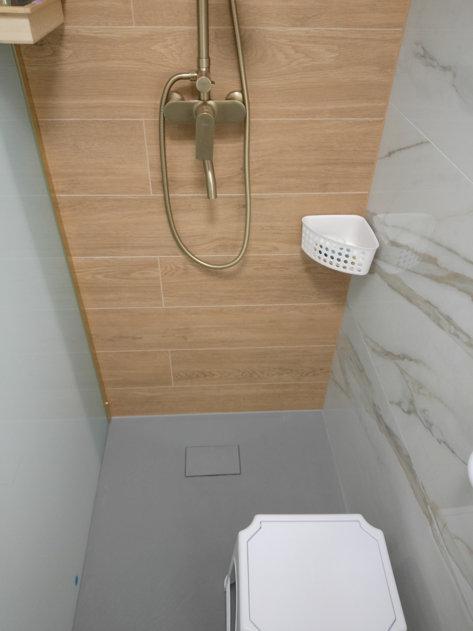 Nowoczesny prysznic z brązową armaturą i drewnopodobnymi płytkami w Koszalinie, z odpływem liniowym w posadzce i narożną półką na kosmetyki.