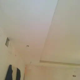 Sufit podwieszany z płyt kartonowo-gipsowych w trakcie montażu, widoczne kable oświetleniowe i ślady po szpachlowaniu na ścianach.