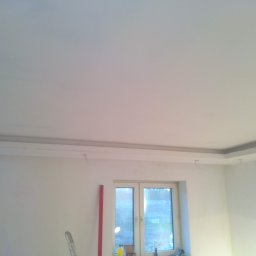 Stel-Bud - Świeżo pomalowane, białe wnętrze pokoju z listwami przysufitowymi i oknem; widoczny fragment drabiny i poziomicy.