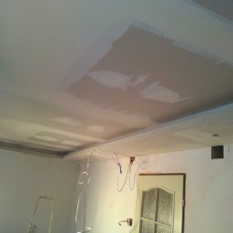 Stel-Bud - Sufit z zamontowaną płytą kartonowo-gipsową w trakcie szpachlowania, widoczne niedoskonałości i ślady po szpachli, wystające kable elektryczne i drabina w tle.