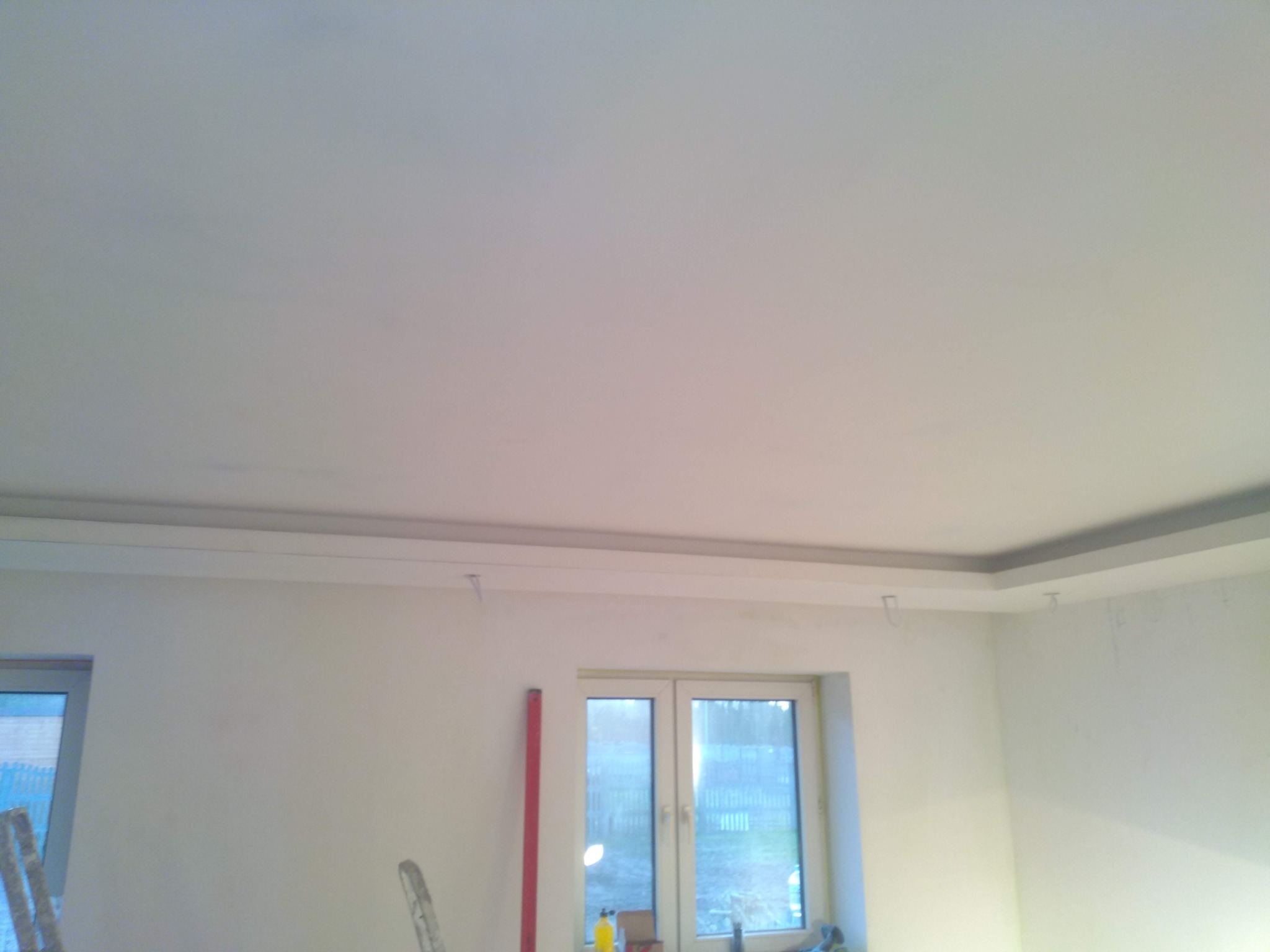 Świeżo pomalowane, białe wnętrze pokoju z listwami przysufitowymi i oknem; widoczny fragment drabiny i poziomicy.