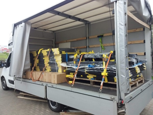 Częściowo załadowana ciężarówka z żółto-czarnymi elementami zabezpieczonymi pasami transportowymi i kartonami, widok z boku na otwartą przestrzeń ładunkową.