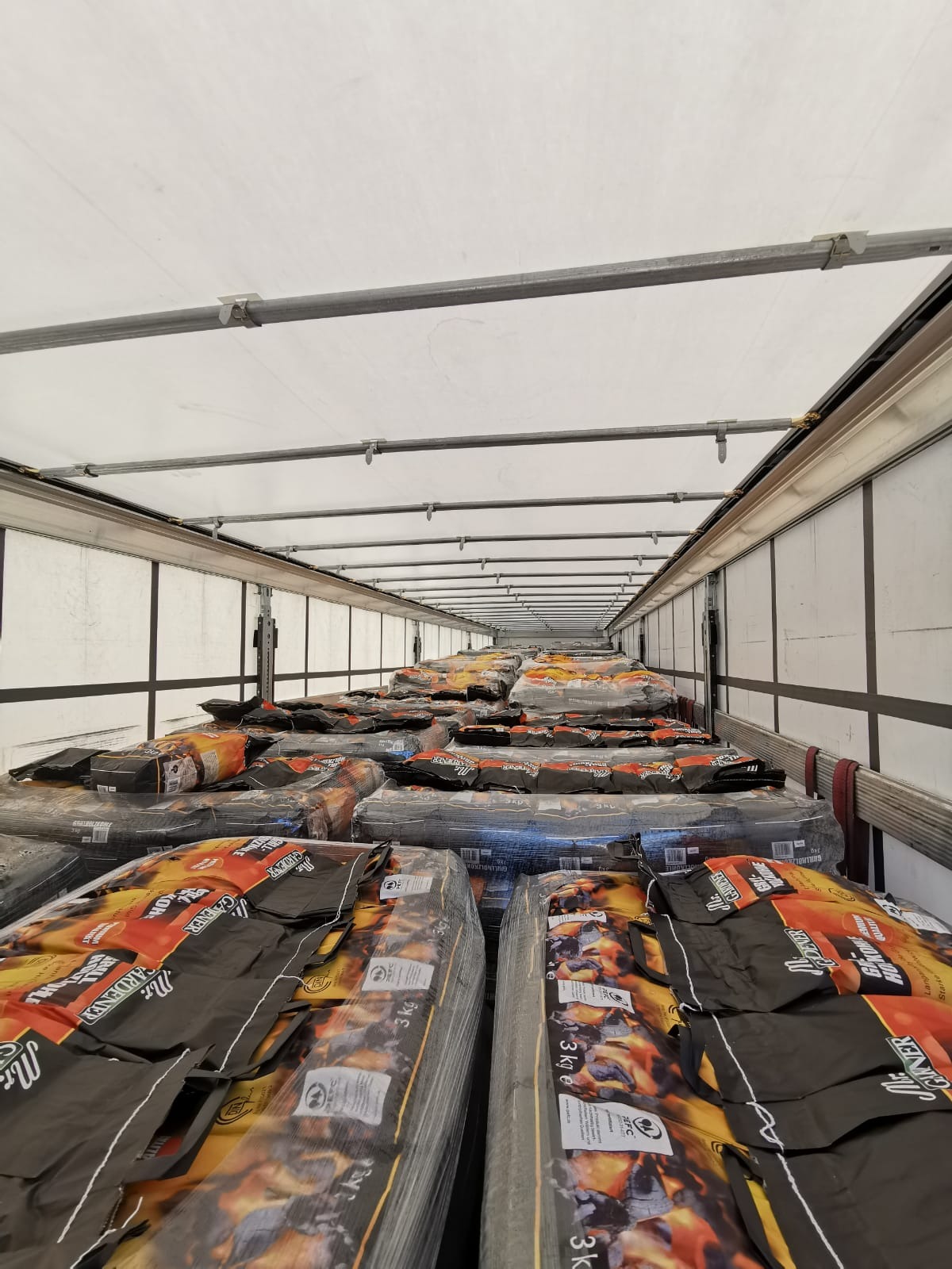 Wnętrze naczepy wypełnione paletami z workami węgla drzewnego marki Mr. Gardener, widok z dołu na sufit naczepy.