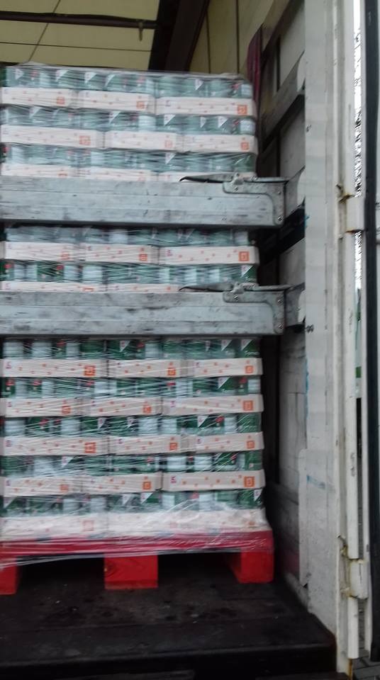 Palety z zapakowanymi produktami, zabezpieczone folią, umieszczone wewnątrz naczepy transportowej z metalowymi uchwytami mocującymi.