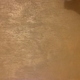 Teksturowana, brązowo-złota ściana wewnętrzna z gniazdkiem elektrycznym w prawym dolnym rogu.