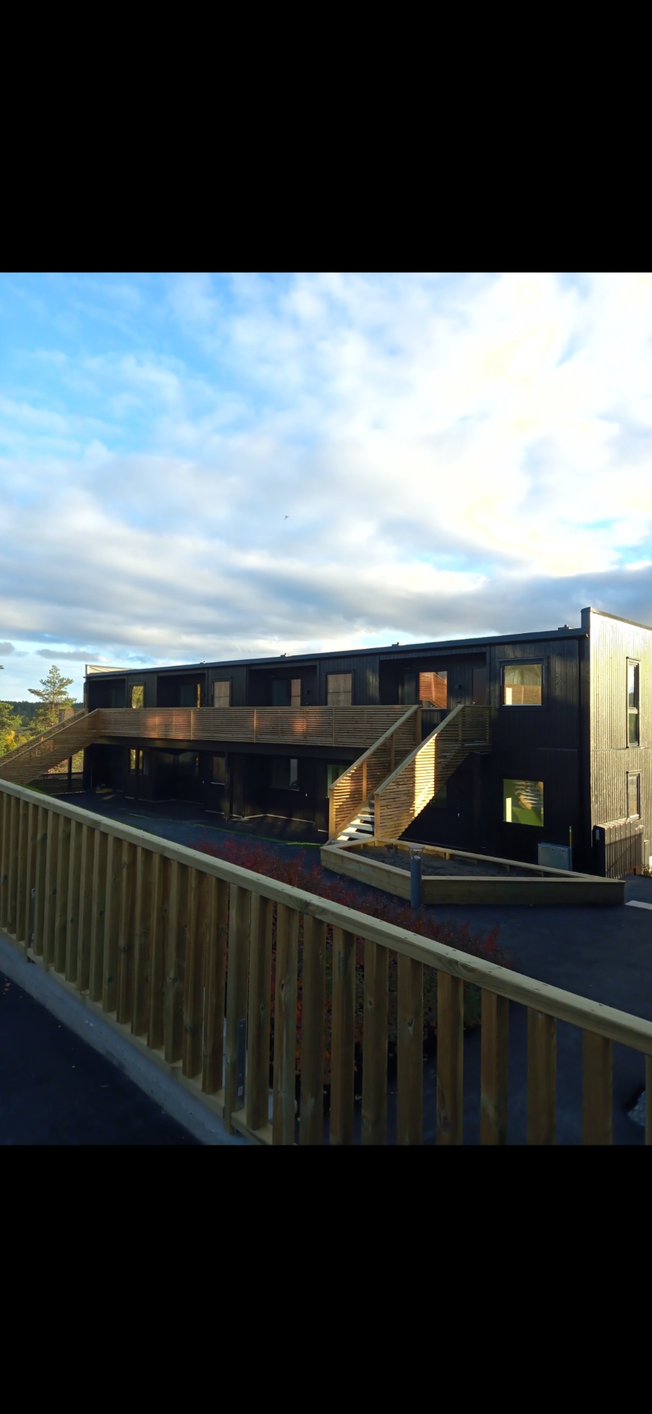 Dwukondygnacyjny, czarny budynek szkieletowy z drewnianymi schodami zewnętrznymi i balustradami. Błękitne niebo z chmurami w tle. Widok z poziomu gruntu.