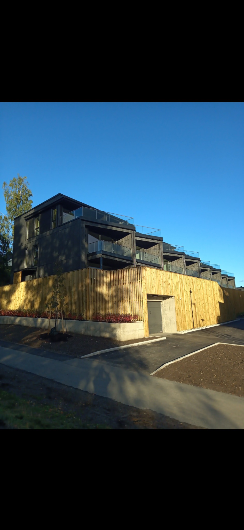 Nowoczesny, trzypiętrowy dom szkieletowy z balkonami i drewnianym ogrodzeniem, widziany z dołu pod kątem. Błękitne niebo w tle.