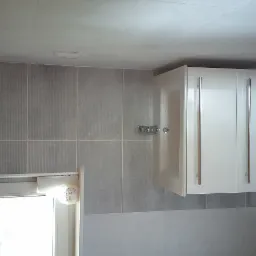 Świeżo wykafelkowana łazienka w Sierakowicach z szarymi płytkami, białą szafką wiszącą i akcesoriami łazienkowymi, widok po remoncie.