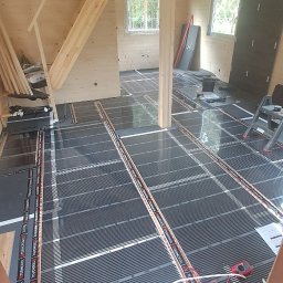 Dream House Ivan Vavryniuk - Montaż folii grzewczej pod podłogę w drewnianym domu, widoczne panele podłogowe i schody w tle.