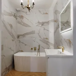Elegancka łazienka po remoncie: marmurowe płytki, złota armatura, drewniana podłoga w jodełkę i designerski żyrandol.
