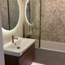 Dream House Ivan Vavryniuk - Nowoczesna łazienka z marmurowymi płytkami, okrągłym lustrem z podświetleniem LED, umywalką z szafką z drewna i kabiną prysznicową ze złotymi elementami.