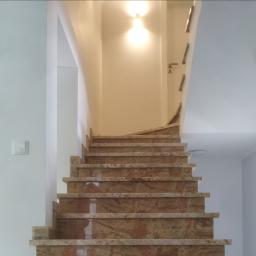 Empire Komfort Life - Wykończone schody wewnętrzne z okładziną imitującą marmur, prowadzące do góry, widoczne oświetlenie i fragment okna.