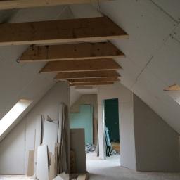 Pawlo ,glazurnictwo z pasją, - Poddasze w trakcie adaptacji: drewniana konstrukcja dachu z izolacją, ściany obłożone płytami gipsowo-kartonowymi, widoczne okno dachowe i materiały budowlane.