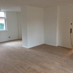 Pawlo ,glazurnictwo z pasją, - Puste, odświeżone wnętrze z panelami podłogowymi w odcieniach brązu, świeżo pomalowanymi białymi ścianami i widocznymi gniazdkami elektrycznymi.