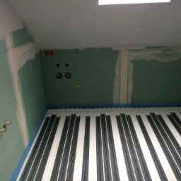Instalacja ogrzewania podłogowego w pomieszczeniu z płytami gipsowo-kartonowymi i wyprowadzonymi instalacjami hydraulicznymi.