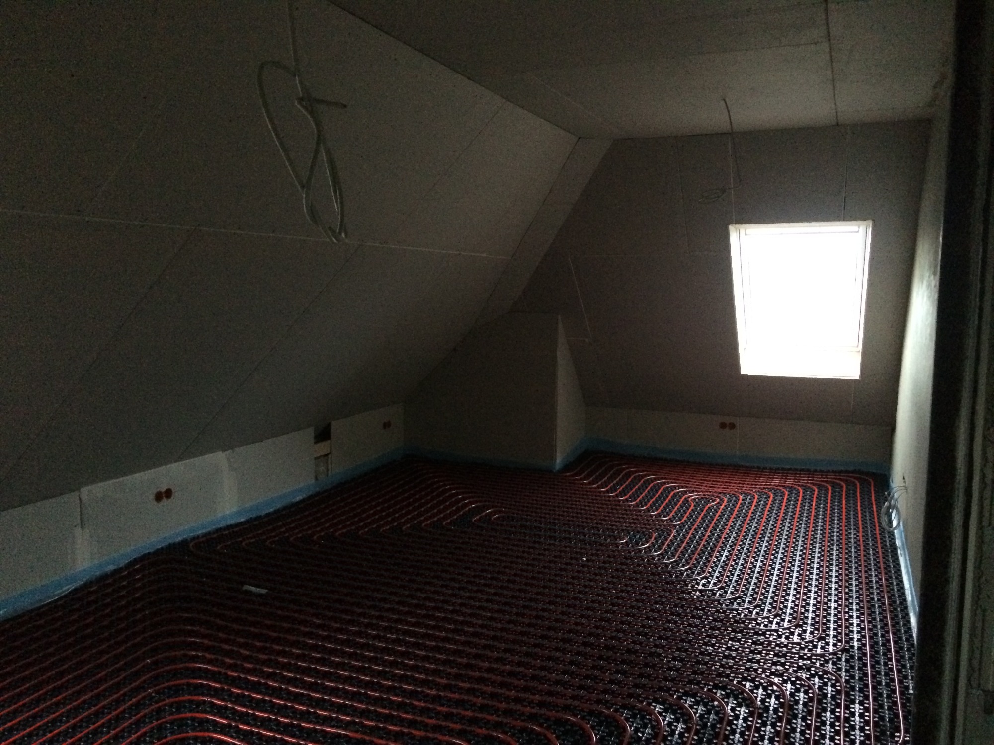Instalacja ogrzewania podłogowego z rur w nowym domu w Żywcu, widok na poddasze ze skosami i małym oknem dachowym.