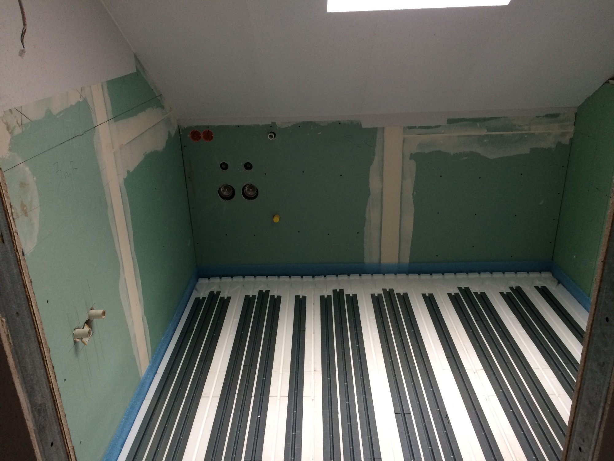 Instalacja ogrzewania podłogowego w pomieszczeniu z płytami gipsowo-kartonowymi i wyprowadzonymi instalacjami hydraulicznymi.