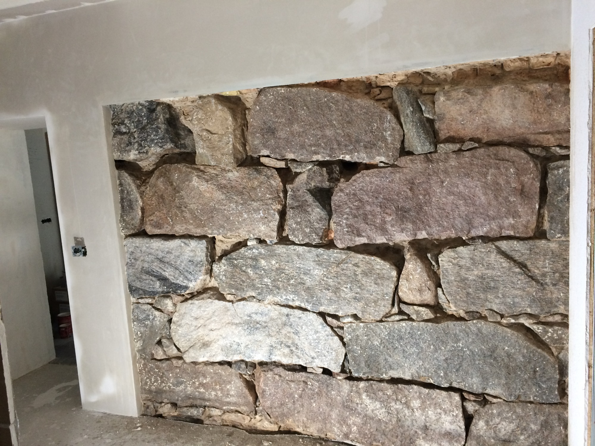 Fragment ściany wewnętrznej wyłożonej nieregularnymi kamieniami różnej wielkości i koloru, z widocznymi śladami zaprawy, obramowany świeżo otynkowanym otworem drzwiowym. Widoczny fragment...