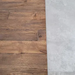 Połączenie podłogi z ciemnego, rustykalnego drewna z szarymi, matowymi płytkami ceramicznymi, widoczne z góry, ukazujące kontrast materiałów i faktur.