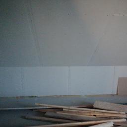 Przedsiębiorstwo MtK - Płyty kartonowo-gipsowe zamontowane na ścianie poddasza, widoczne łączenia i ślady po wkrętach, na podłodze leżą drewniane listwy i fragmenty płyt.