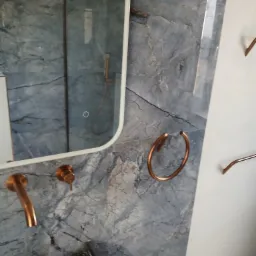 Wykończona łazienka z marmurową ścianą, lustrem i miedzianą armaturą. Nowoczesny design z akcentami miedzi i szarości. Eleganckie wykończenie.