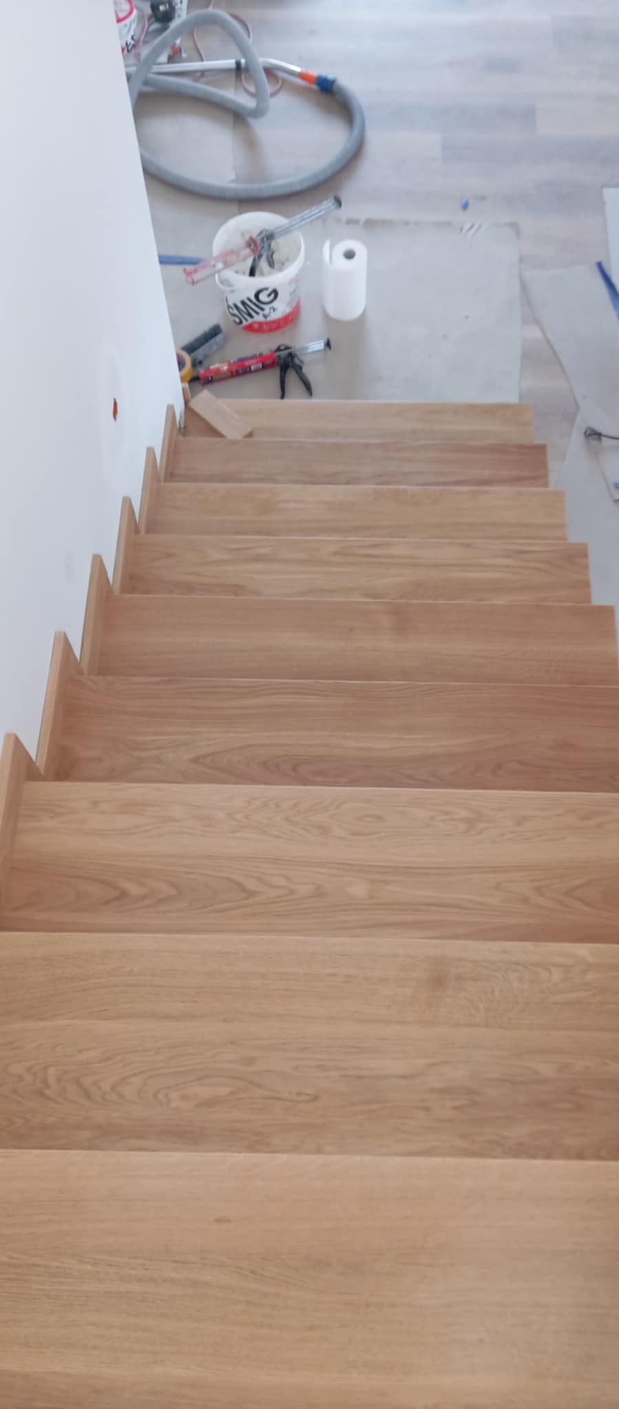 Drewniane schody z widocznymi narzędziami pracy i akcesoriami na górze, ukazujące etap montażu lub wykończenia, z bliska.