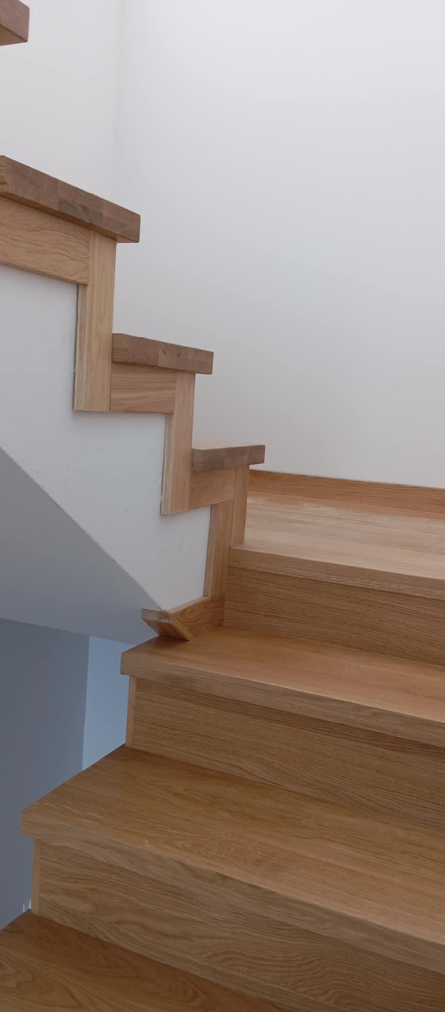 Drewniane schody o jasnym odcieniu dębu, z widocznymi detalami łączeń i minimalistycznym wykończeniem, osadzone w białym wnętrzu z delikatnym oświetleniem.