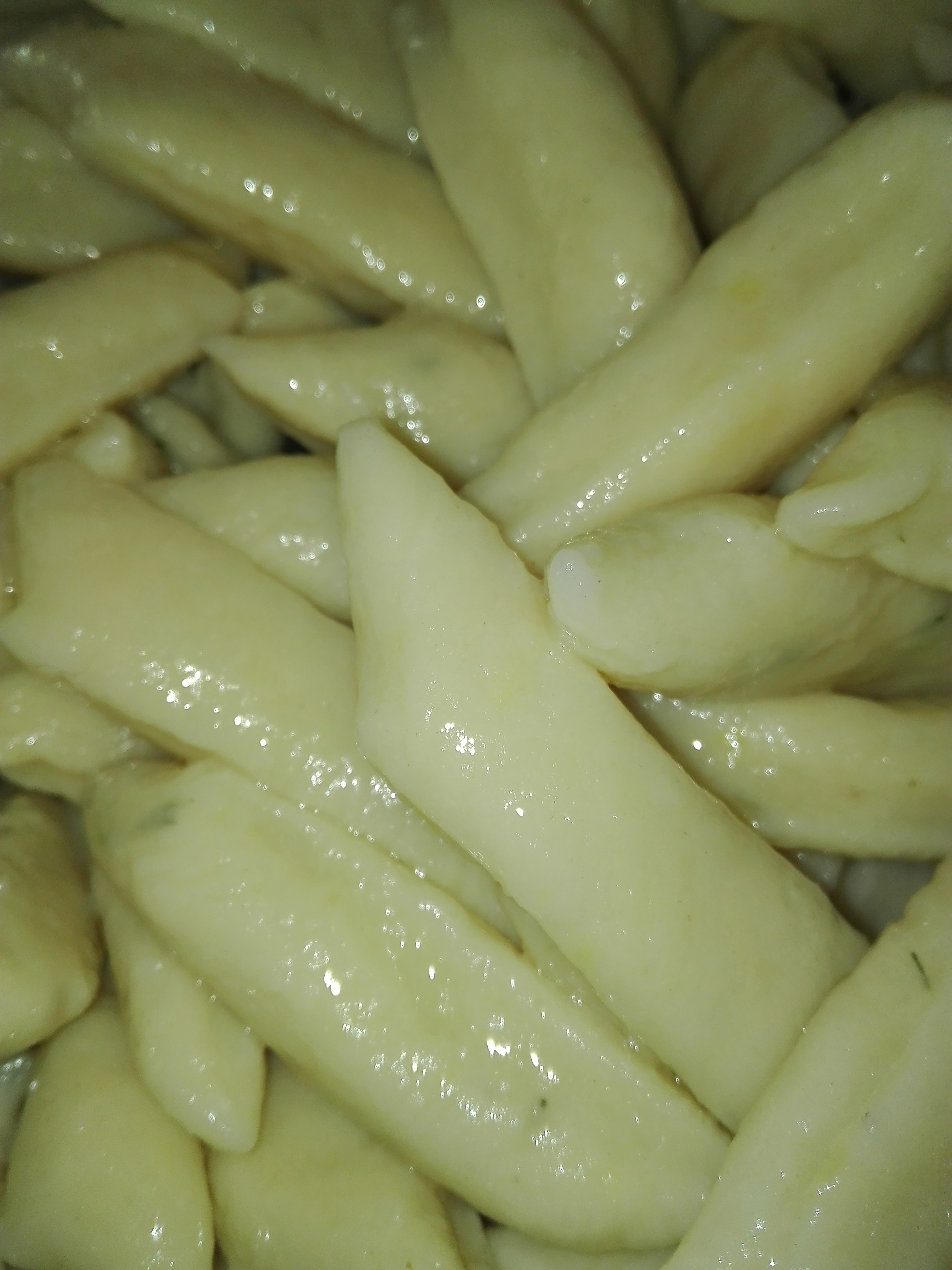 Jasne, gotowane kopytka ułożone blisko siebie, widoczne delikatne odbicia światła na ich powierzchni.