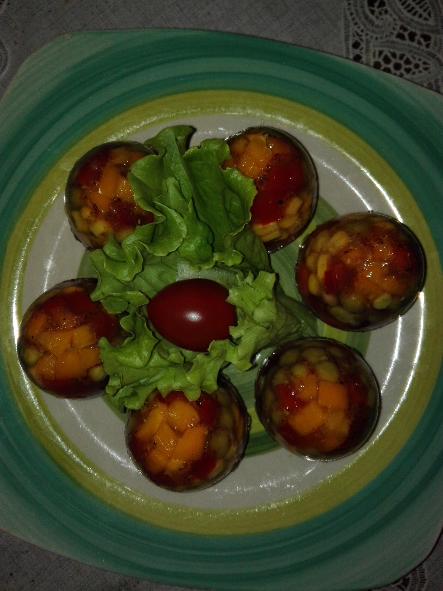 Deser w galarecie z kawałkami owoców i warzyw, podany na talerzu z zielonymi paskami, udekorowany sałatą i pomidorkiem koktajlowym.