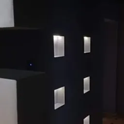 Czarna ściana z sześcioma podświetlanymi, kwadratowymi wnękami, parkiet na podłodze.