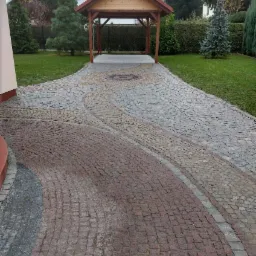 Ułożona z kostki granitowej aleja w ogrodzie z drewnianą altaną w tle, wzór z czerwono-szarych kostek, widok z góry.