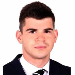 Portret młodego mężczyzny w ciemnym garniturze i krawacie w czarno-białe wzory na białym tle.