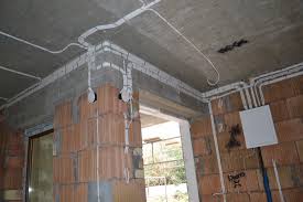 Rozprowadzenie przewodów elektrycznych natynkowo w surowym pomieszczeniu z cegły, widoczna puszka elektryczna i wystające przewody.