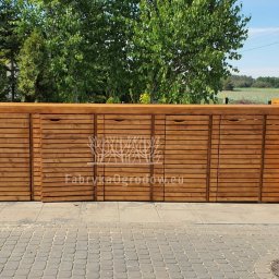 Fabryka Ogrodów Filip Michał Młynarczuk - Drewniana zabudowa śmietnikowa z lamelami, zintegrowana z ogrodzeniem, na tle zieleni. Estetyczne rozwiązanie do przechowywania pojemników na odpady.