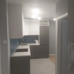 Nowoczesna kuchnia w szaro-białej tonacji z niebieskim akcentem na ścianie nad blatem, widok z perspektywy wejścia do pomieszczenia, oświetlenie punktowe w suficie.