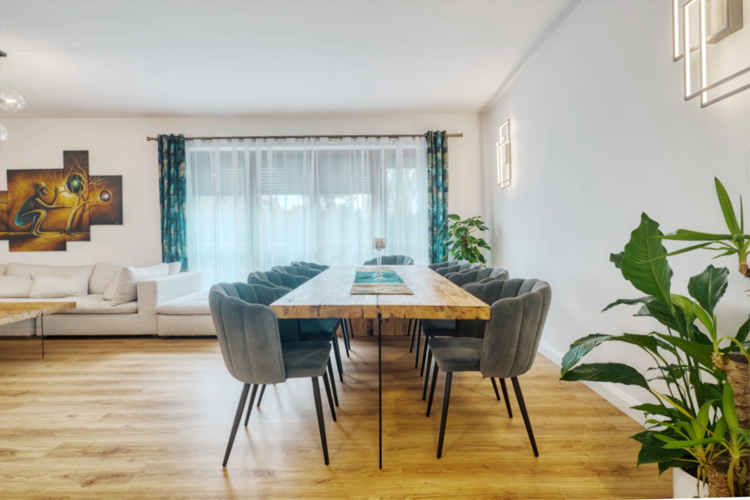 Jasne wnętrze jadalni z drewnianym stołem, szarymi krzesłami, parkietem i obrazem na ścianie.