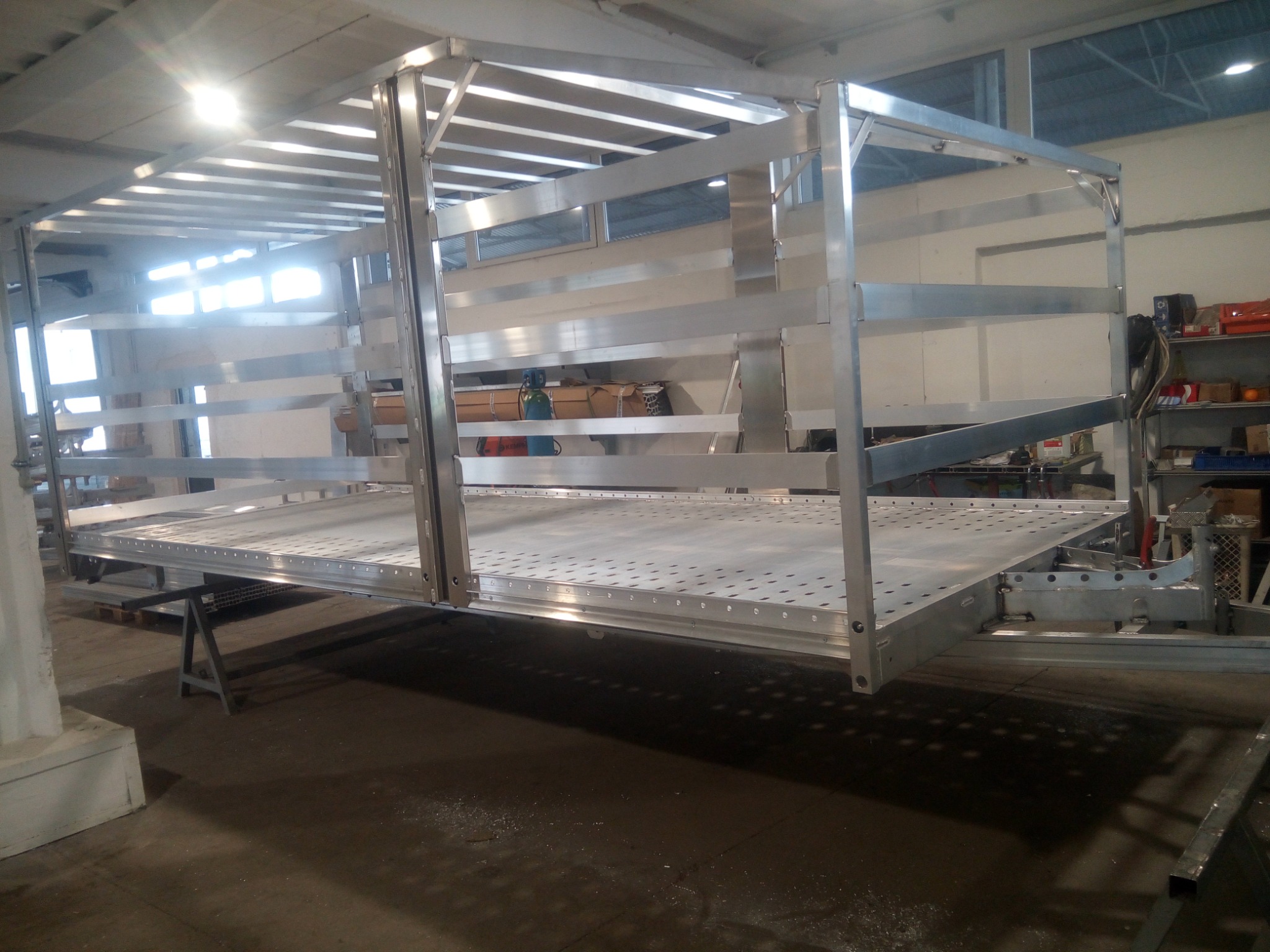 Metalowa konstrukcja hali w surowym stanie, widoczne spawane elementy i perforowana podłoga, oświetlenie górne odbija się od gładkich powierzchni.