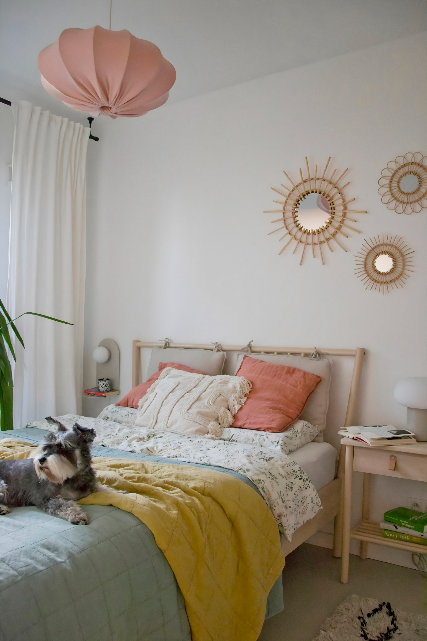 Jasna sypialnia z drewnianym łóżkiem, pastelową pościelą, okrągłymi lustrami na ścianie i psem rasy sznaucer miniaturowy leżącym na łóżku.