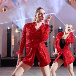 Paczka Events - Dwie tancerki w czerwonych, cekinowych kostiumach na scenie z oświetleniem punktowym i głośnikami w tle, wykonujące synchroniczny układ taneczny.