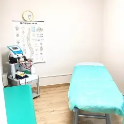 Gabinet z leżanką przykrytą turkusowym prześcieradłem, aparaturą do elektroterapii na wózku i plakatem z układem kręgosłupa na ścianie.