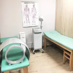 Gabinet rehabilitacyjny z aparaturą do magnetoterapii, leżanką i plakatem anatomicznym na ścianie.