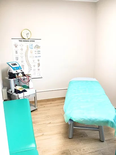 Gabinet z leżanką przykrytą turkusowym prześcieradłem, aparaturą do elektroterapii na wózku i plakatem z układem kręgosłupa na ścianie.