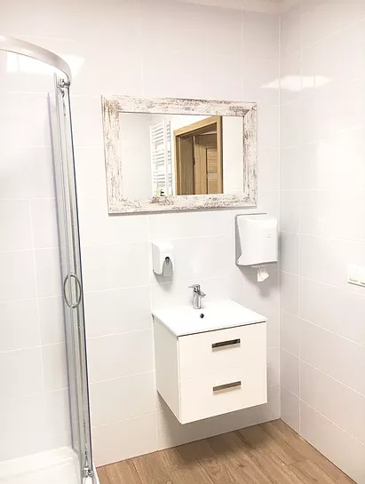 Nowoczesna łazienka z kabiną prysznicową, wiszącą szafką z umywalką i lustrem w drewnianej ramie z efektem postarzania, widok na grzejnik drabinkowy w odbiciu lustra.