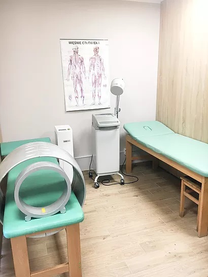 Gabinet rehabilitacyjny z aparaturą do magnetoterapii, leżanką i plakatem anatomicznym na ścianie.