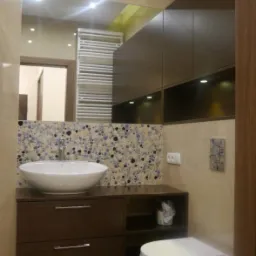 Nowoczesna łazienka w Przywidzu z umywalką nablatową na szafce z ciemnego drewna, toaletą wiszącą i bidetem. Nad umywalką lustro z podświetleniem i grzejnik drabinkowy.