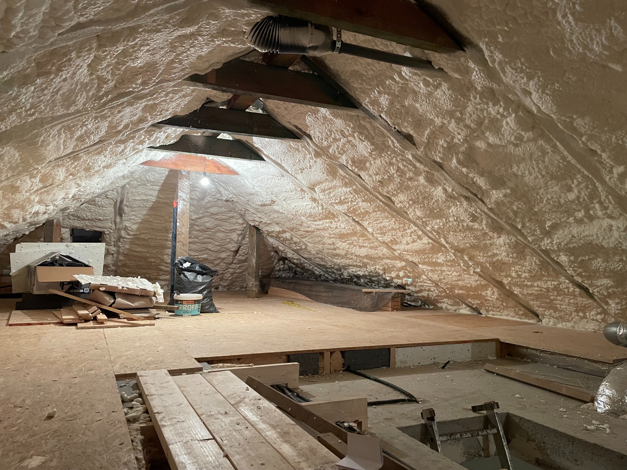 Poddasze ocieplone pianką PUR, widoczne drewniane elementy konstrukcji, fragment wentylacji i materiały budowlane na podłodze.