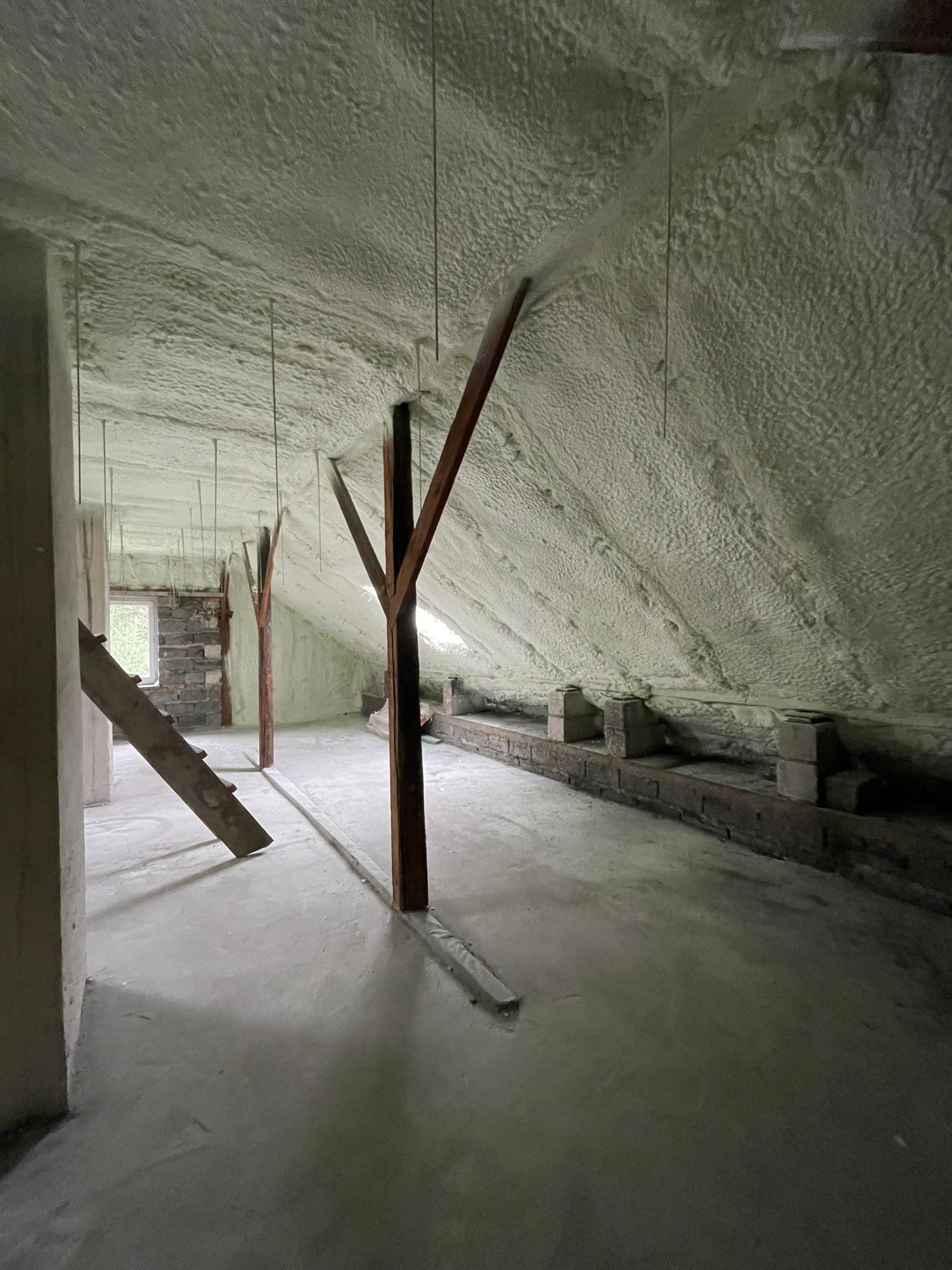 Poddasze po ociepleniu pianką PUR, widoczne drewniane elementy konstrukcyjne i wystające metalowe pręty z sufitu, ściany z fragmentami cegieł.