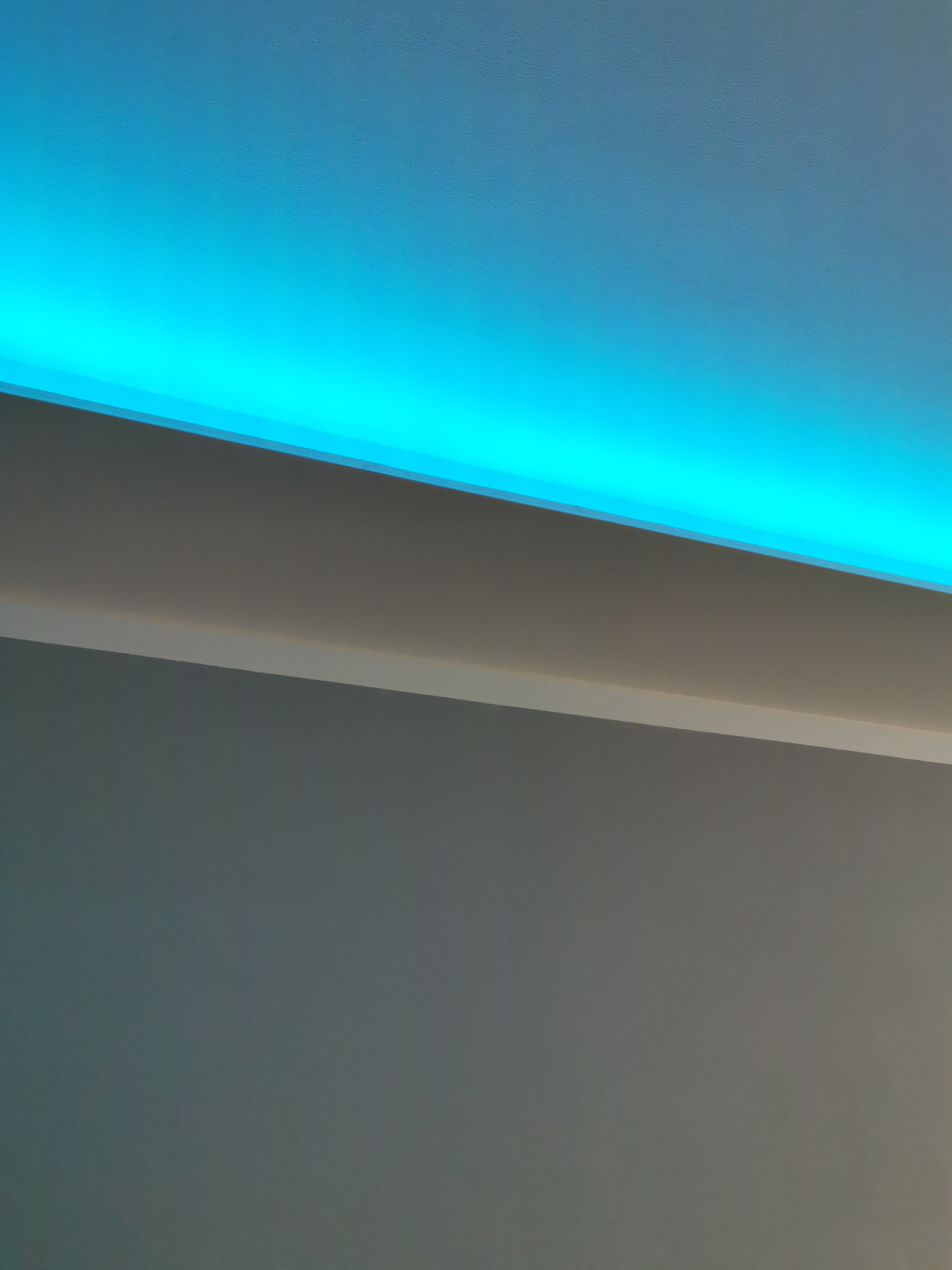 Niebieskie oświetlenie LED w suficie podwieszanym, szara ściana poniżej.